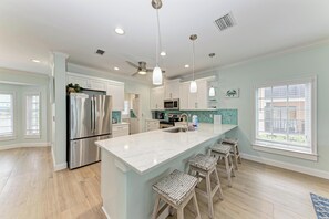 A modern kitchen with a central island, stainless steel appliances, pendant lighting, and a view of the outside.