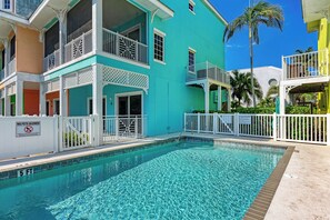 A pool area with a no pets allowed sign, a clear blue pool, and colorful buildings with balconies.