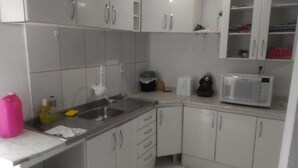 Una pequeña cocina con armarios blancos, un lavamanos, un microondas y un cubo de basura.