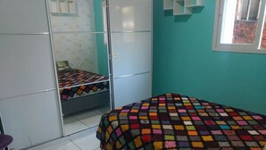Un dormitorio con una cama cubierta por una manta de crochet colorida, un armario y una ventana con vista a un muro de ladrillos.