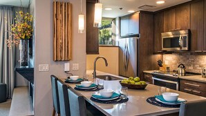 A modern kitchen with a central island, stainless steel appliances, and a view of greenery outside.