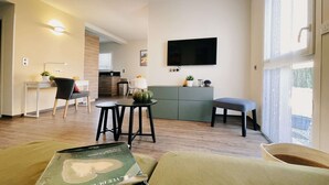 Un soggiorno moderno con un divano, un tavolino e una zona pranzo con tavolo e sedie. È presente anche un angolo cottura con un bancone e mobili, e una TV montata a parete.