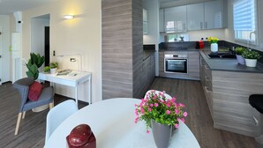 Una cucina moderna con elettrodomestici integrati, una zona pranzo con tavolo e sedie bianche e un piccolo spazio ufficio con scrivania e sedia.