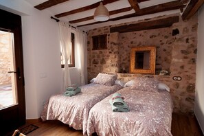 Two single beds with matching patterned bedding, a stone wall, and wooden ceiling with exposed beams.