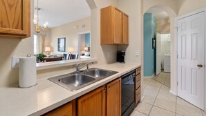 A kitchen with a double sink, wooden cabinets, a dishwasher, and a coffee maker. - Windsor Hills Resort Condo-Disney, Golf, and Fun! (Kissimmee)