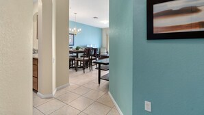 A hallway leading to a dining area with a chandelier, a framed picture on the wall, and a light blue wall. - Windsor Hills Resort Condo-Disney, Golf, and Fun! (Kissimmee)