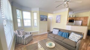 A living room with a sofa, a coffee table, a striped chair, and a view of the kitchen. - Orlando Oasis II - Pool Open! Clean Spacious Villa By Disney (Kissimmee)