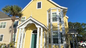 A yellow house with a green door and white trim, surrounded by palm trees and other vegetation. - Orlando Oasis II - Pool Open! Clean Spacious Villa By Disney (Kissimmee)