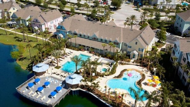 An aerial view of a resort with a large swimming pool, a dock with lounge chairs, and a variety of buildings. - Orlando Oasis II - Pool Open! Clean Spacious Villa By Disney (Kissimmee)