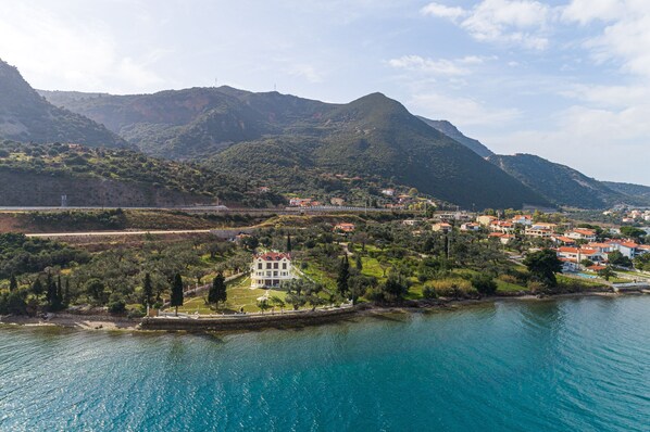 A coastal town with a prominent white building surrounded by greenery and mountains in the background. - Villa Filoxenia - by the sea - up to 12 guests (Aigialeia)