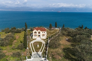 A large, white building with a red roof, surrounded by a well-maintained garden and a view of the sea. - Villa Filoxenia - by the sea - up to 12 guests (Aigialeia)