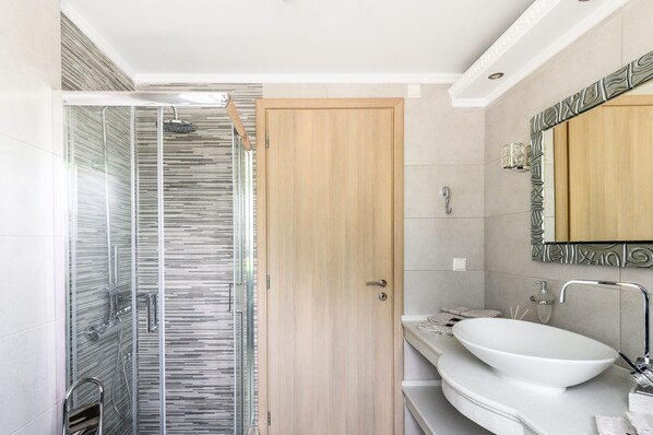 Une salle de bain moderne avec une douche à parois de verre, une porte en bois et un lavabo blanc avec un miroir au-dessus.