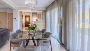 A modern dining area with a glass table, grey upholstered chairs, and a chandelier. - Villa Filoxenia - by the sea - up to 12 guests (Aigialeia)