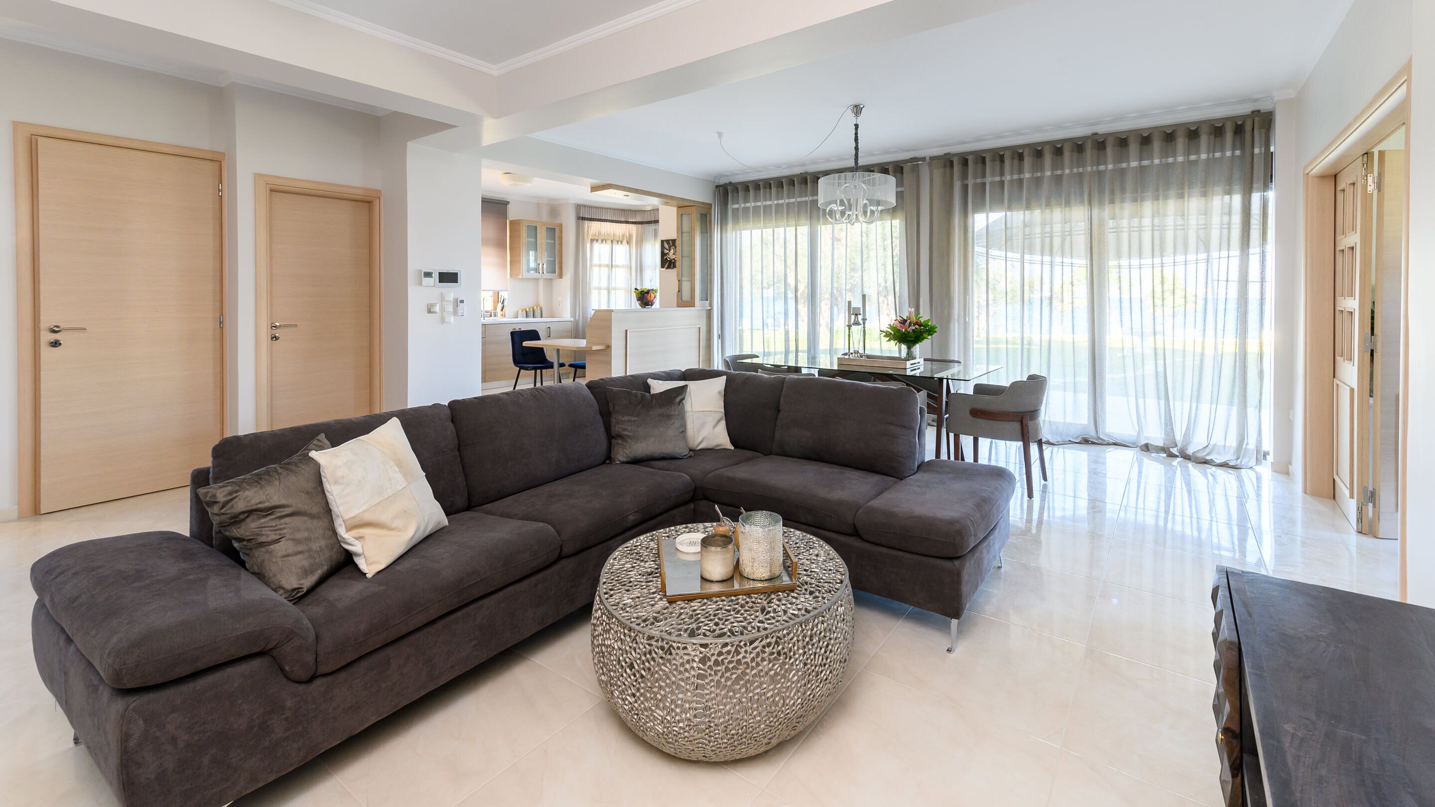 Uma sala de estar moderna com um sofá seccional, uma mesa de centro redonda e uma área de jantar com mesa e cadeiras.