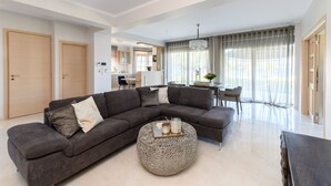 A modern living room with a sectional sofa, a round coffee table, and a dining area with a table and chairs. - Villa Filoxenia - by the sea - up to 12 guests (Aigialeia)