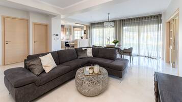 Uma sala de estar moderna com um sofá seccional, uma mesa de centro redonda e uma área de jantar com mesa e cadeiras.