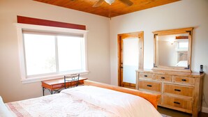 Ein Schlafzimmer mit Bett, Schreibtisch, Stuhl, Kommode und einem großen Fenster.
