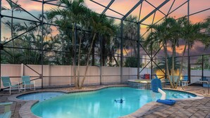 An indoor swimming pool with a view of palm trees and a sunset. - Sabal Palms is a spectacular luxury pool home across from beach with Gulf view (Fort Myers Beach)