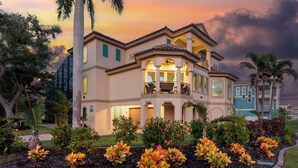 A large, multi-story house with a balcony, surrounded by landscaped gardens and palm trees. - Sabal Palms is a spectacular luxury pool home across from beach with Gulf view (Fort Myers Beach)