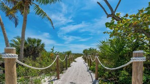 A sandy pathway bordered by wooden posts with rope barriers, surrounded by palm trees and tropical vegetation. - Sabal Palms is a spectacular luxury pool home across from beach with Gulf view (Fort Myers Beach)