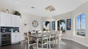 Een moderne keuken met witte kastjes, een eethoek met een houten tafel en stoelen, en grote ramen met uitzicht op de oceaan.
