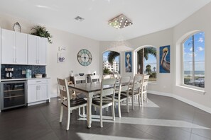 A modern kitchen with white cabinets, a dining area with a wooden table and chairs, and large windows with a view of the ocean.