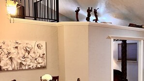 A dining area with a wooden table and chairs, a floral painting on the wall, and a staircase leading to an upper level. - Beautiful and Relaxing Guest House!! (Redding)
