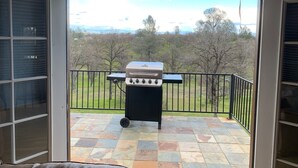 A balcony with a grill, a view of a grassy area, and a stone-tiled floor. - Beautiful and Relaxing Guest House!! (Redding)
