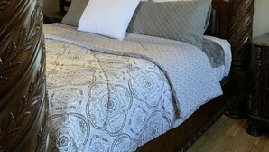 A four-poster bed with a patterned bedspread and pillows, a wooden headboard, and a nightstand with a lamp. - Beautiful and Relaxing Guest House!! (Redding)