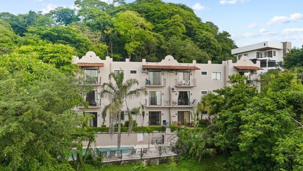A multi-story building with balconies, surrounded by lush greenery and a pool. - Stylish + Fast Wifi+ IPTV+ Fully Equipped (Tamarindo)