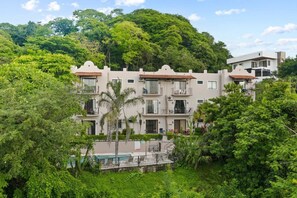 A multi-story building with balconies, surrounded by lush greenery and a pool. - Stylish + Fast Wifi+ IPTV+ Fully Equipped (Tamarindo)