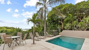 A poolside area with lounge chairs and a table, surrounded by lush greenery and a view of the ocean. - Stylish + Fast Wifi+ IPTV+ Fully Equipped (Tamarindo)