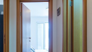 A hallway with wooden flooring leading to a bedroom with a bed and a window. - Apartment Blue (Budva)