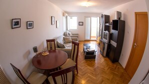 A compact living space with a dining area, sofa, and entertainment unit. - Apartment Blue (Budva)