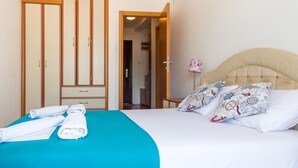 A hotel room with a bed, a blue bedspread, white pillows, and a wooden wardrobe. - Apartment Blue (Budva)