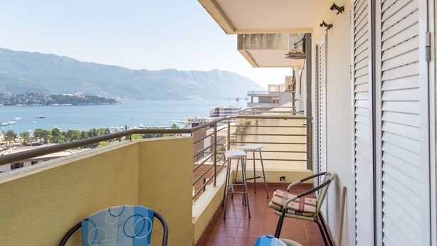 A balcony with a table and chairs, overlooking a body of water and distant mountains. - Apartment Blue (Budva)