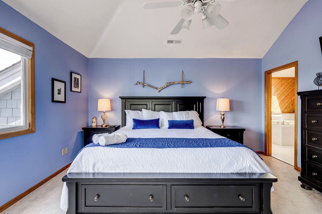 A bedroom with a bed, two bedside tables, a ceiling fan, and a view of the bathroom.