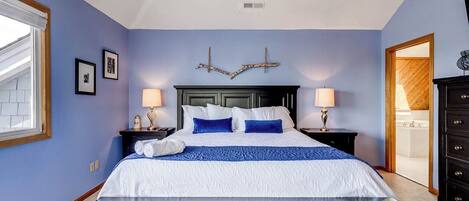 A bedroom with a bed, two bedside tables, a ceiling fan, and a view of the bathroom.