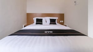 Une chambre d’hôtel avec un lit simple, une tête de lit en bois et une couvre-lit noir et blanc sur laquelle on peut voir le nom de la marque « OYO ».