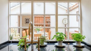 A kitchen with a large window, a scale, and potted plants on the counter.