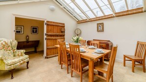 A conservatory with a dining table set for six, surrounded by wooden chairs.