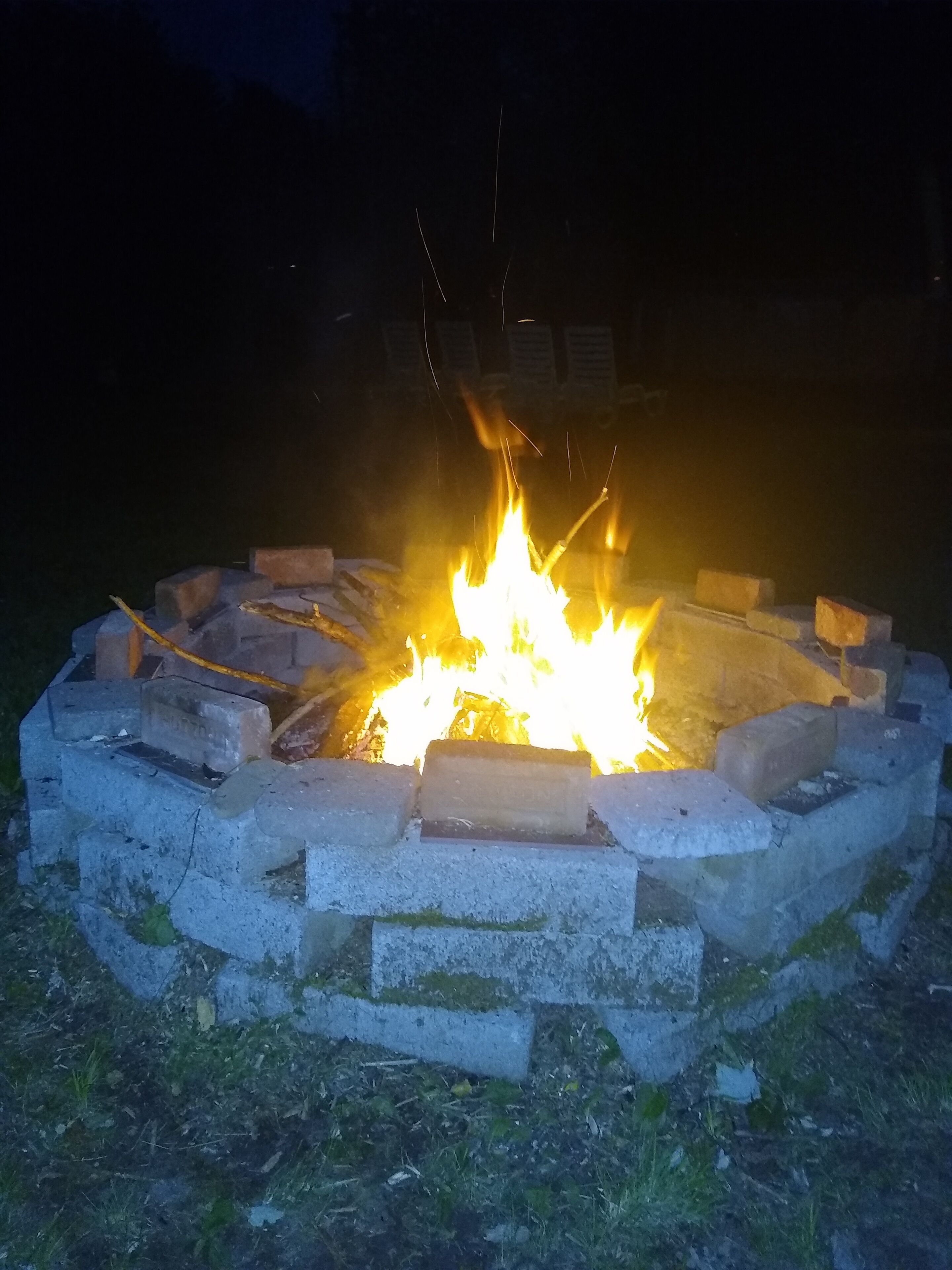 A campfire in a circular stone fire pit surrounded by grass.