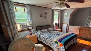 A bedroom with a bed, two wicker chairs, a ceiling fan, and a window with curtains.