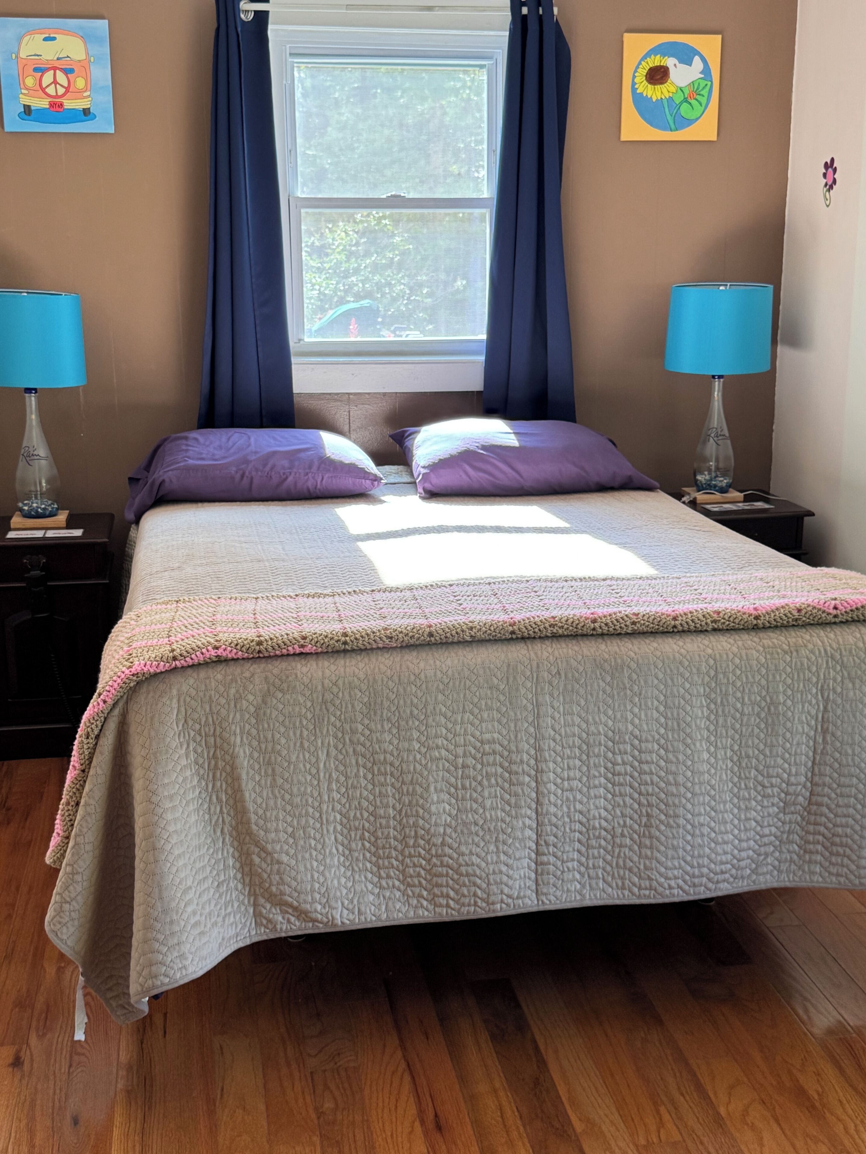 Un dormitorio con cama, dos mesitas de noche, una ventana con cortinas y una obra de arte en la pared.
