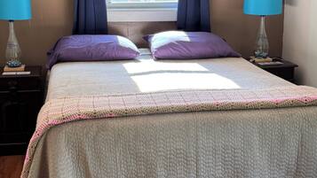 Un dormitorio con cama, dos mesitas de noche, una ventana con cortinas y una obra de arte en la pared.