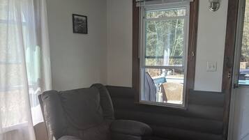 Un salón acogedor con un sillón de cuero, un ventanal con persianas y suelo de madera.