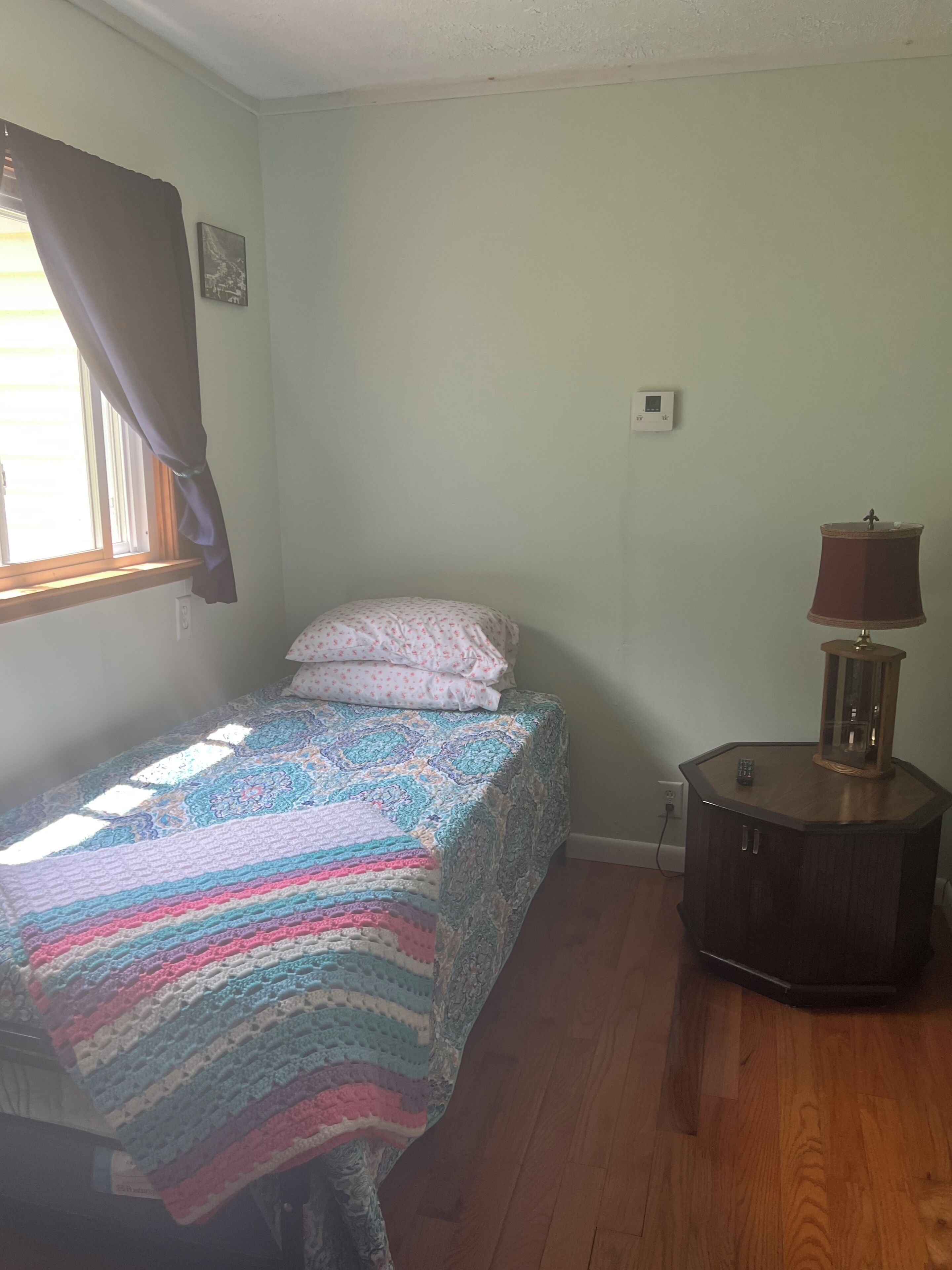 Un dormitorio con cama, mesita de noche, lámpara y ventana con cortinas.
