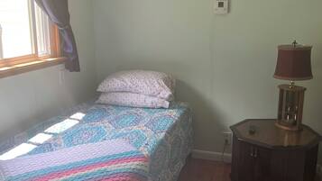 Un dormitorio con cama, mesita de noche, lámpara y ventana con cortinas.