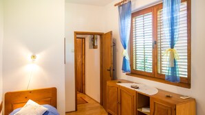 A bedroom with a wooden bed, a bedside table, a wardrobe, and a window with curtains. - Apartment Azur (Budva)