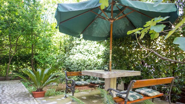 A patio area with a table and benches, surrounded by greenery. - Apartment Azur (Budva)